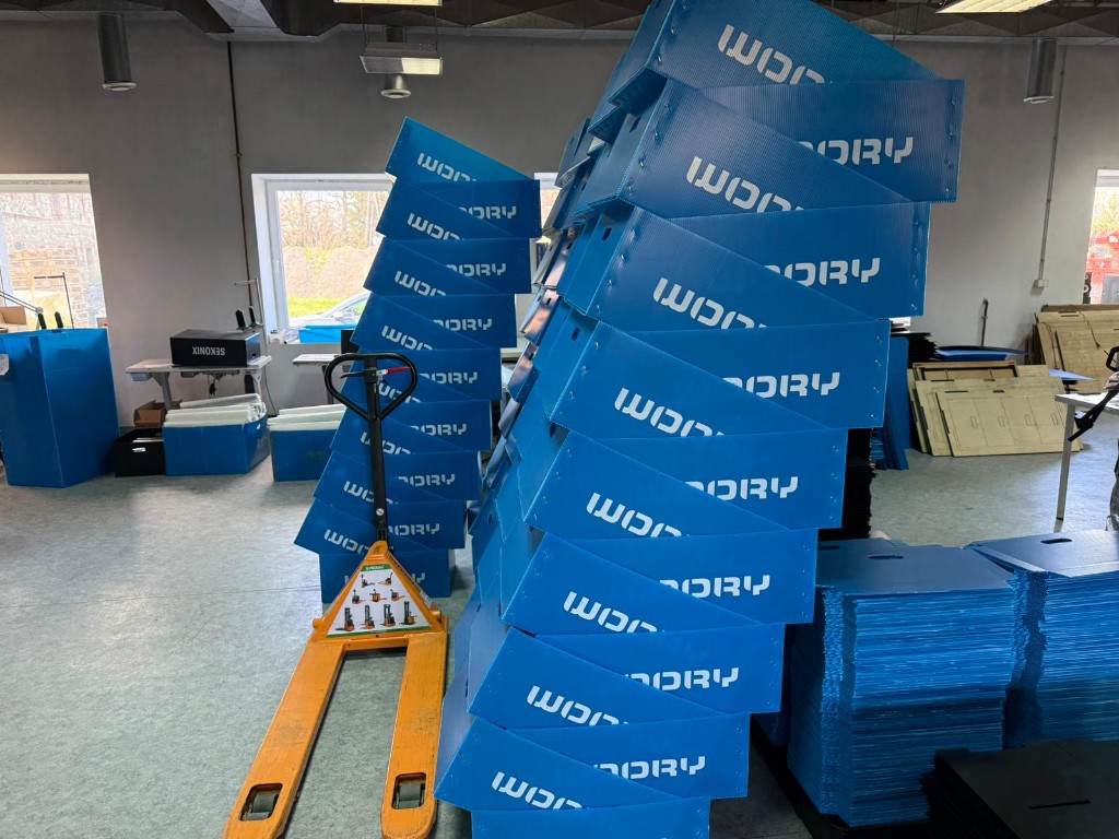 Blue corrugated plastic boxes staged in a workshop with a pallet jack.