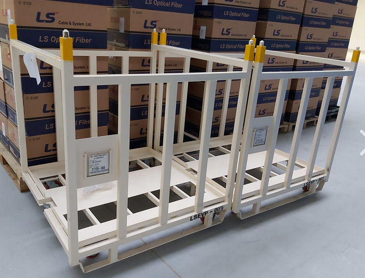 Two industrial metal trolleys with red casters and cage sides in a warehouse beside stacked cartons.