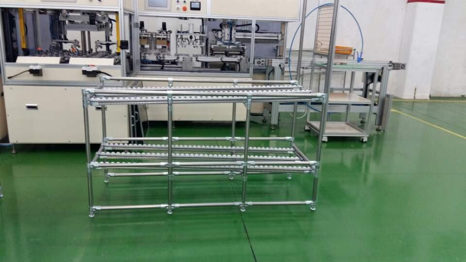 Modular pipe-and-joint FIFO gravity rack with white roller tracks on a factory floor.