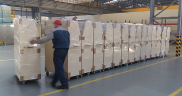 Row of tall shrink-wrapped mobile racks on a polished factory floor with a yellow safety line.