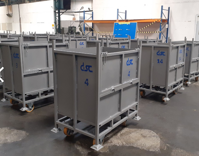 Rows of heavy-duty grey metal mobile bins on orange casters in a large warehouse.
